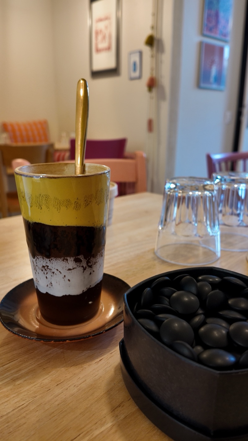 un bol de pierres noires et un café dans un verre jaune, la salle de Fricotte en fond